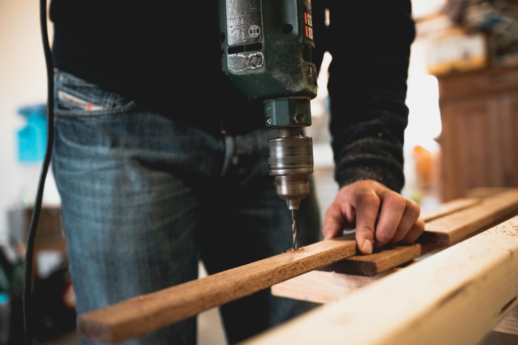 pexels-photo-1094767-1094767 Close-up of a person using an electric drill on a wooden plank, showcasing detailed woodworking skills.